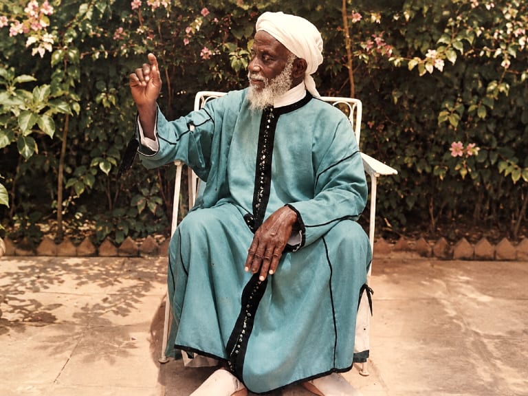Le marabout Saraba, assis dans son patio, la main levée pendant une consultation